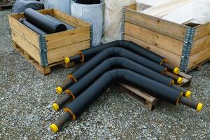 Angled insulated heating pipes with yellow plastic plugs lie on the construction site. photo