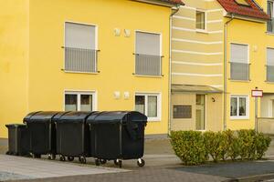 Black trash containers standing near a apartment building. photo