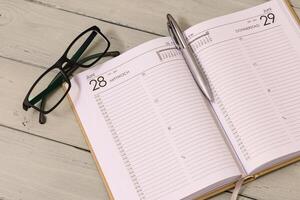 Lying on the table, an open schedule - planner with an auto pen and glasses nearby. photo