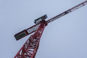 Bottom view of a construction crane cabin and part of an arrow against a sky. photo