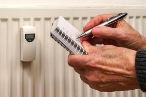 del hombre manos grabación calor consumo lecturas en un calefacción radiador foto