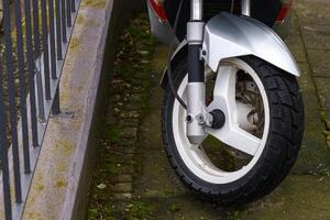 The front wheel of a motor scooter standing on the sidewalk. photo