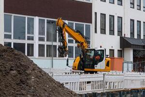 amarillo excavador a un construcción sitio en contra un edificio. foto