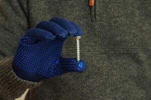 Man hand in blue gloves holding a large metal bolt. Close up. photo