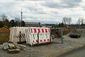 White and red plastic fencing at a construction site next to an excavator bucket and a cut pipe. photo