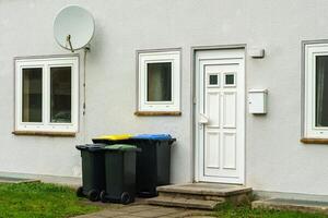 el plastico basura latas cerca el Entrada a un residencial edificio. satélite plato en el pared foto