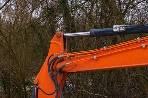 The hydraulic part of the excavator boom against the background of tree branches photo