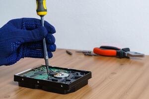 The hand of a man in a glove is repairing a hard disk of a personal computer with a screwdriver. photo