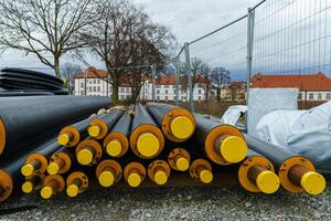 Black isolated heating large pipes with yellow plastic plugs lie on a construction site. photo