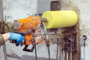 Worker using an electric drill to make a hole in a concrete wall, closeup photo