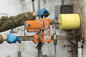 Worker using an electric drill to make a hole in a concrete wall, closeup photo