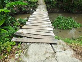 Turismo de un rural escena con un antiguo de madera puente cruce un marrón agua río foto