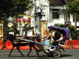 Surakarta, Central Java, Indonesia April 11, 2024. A horse drawn carriage with local tourist passing on Jalan Adisucipto near Manahan Stadium at Surakarta City, Central Java, Indonesia photo