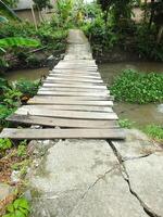 sightseeing of a rural scene with an old wooden bridge crossing a brown water river photo