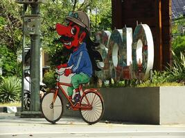 Surakarta, abril 11 2024, ciudad caminar con el palabras solo y un Wayang mascota alrededor manahan estadio. icónico punto de referencia Wayang personaje montando un bicicleta. foto