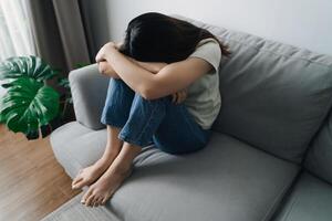 Unhappy lonely depressed woman is sitting on the couch and covering her face with her hands photo