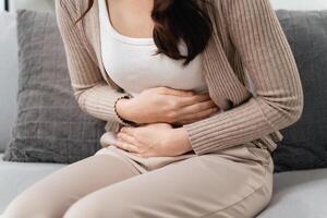 The woman with a stomachache is holding her stomach in pain, sitting on the sofa in the living room. photo