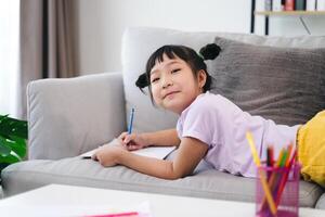 un joven niña es sentado en un sofá con un lápiz y un cuaderno foto