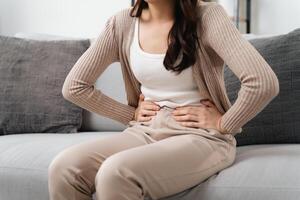 The woman with a stomachache is holding her stomach in pain, sitting on the sofa in the living room. photo