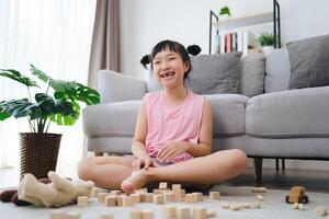un pequeño niña se sienta en el piso jugando con de madera bloques foto