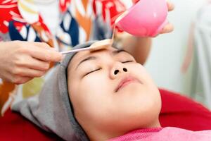 Beautiful young Asian woman getting a facial mask treatment at the beauty salon. Facial skincare. photo