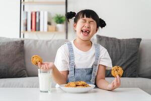 un joven niña es comiendo galletas y Bebiendo Leche foto