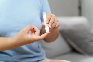 Asian woman using lancet on finger for checking blood sugar level by Glucose meter photo