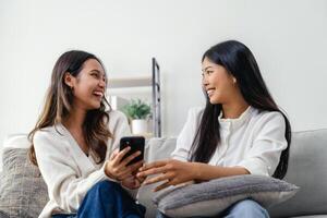 Two women sitting on a couch, one holding a cell phone, talking, smiling, and laughing. photo