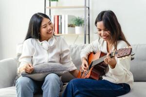 Two women are sitting on a couch, one of them playing a guitar photo