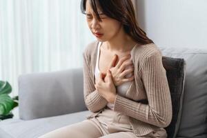 A woman is sitting on a couch with her hand holding on her chest, suffering from a heart attack. photo