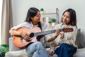 Two women are sitting on a couch, one of them playing a guitar photo