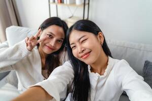 dos mujer son sonriente y tomando un selfie sentado en el sofá en el vivo habitación a hogar. foto