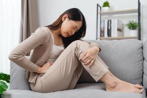 The woman with a stomachache is holding her stomach in pain, sitting on the sofa in the living room. photo