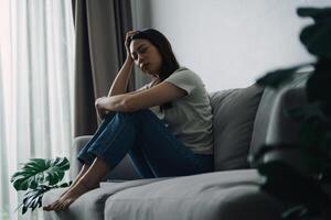 Unhappy lonely depressed woman is sitting on the couch and holding her head. photo