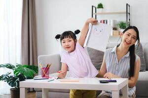 A young girl is sitting at a table with a drawing of a face in front of her photo