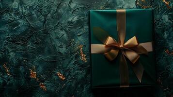 Dark green gift box with elegant gold ribbon on dark background. Greeting gift with copy space for Christmas present, holiday or birthday photo