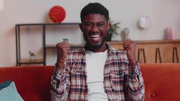 Young adult man shouting, raising fists in gesture I did it, celebrating success, winning at home video