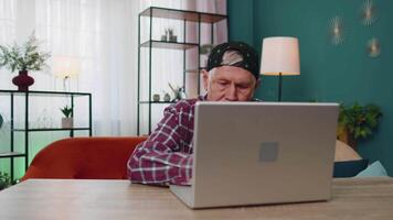 Senior grandfather man using laptop computer, typing at home room, looking at camera, smiling video