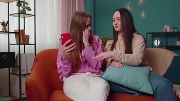 glad flickor vänner syskon tittar på foton på smartphone på soffa på Hem, njut av social media video