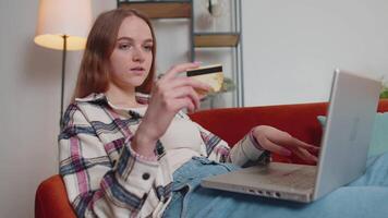 Woman sitting at home using credit bank card and laptop pc while transferring money online shopping video