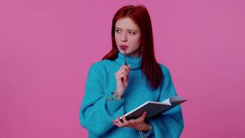 Pensive ginger woman making notes, writing down thoughts with pen into notepad notebook diary indoor video