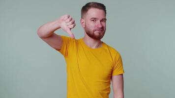 Upset man in casual t-shirt showing thumbs down sign gesture, disapproval, dissatisfied dislike video