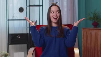 Excited amazed young woman raising hands in surprise shocked by sudden victory at home on chair video