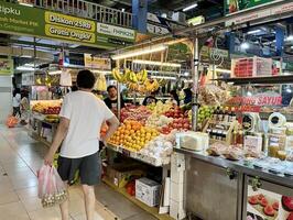 Jakarta, Indonesia - May 24th, 2024 - Indoor fresh market fruit bazaar display store with a few buyers and sellers isolated on horizontal ratio indoor market stall background. photo