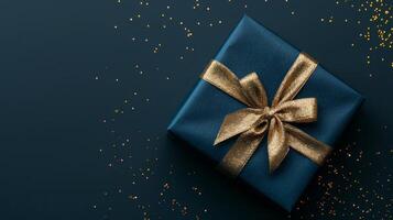 Dark blue gift box with elegant gold ribbon on dark background. Greeting gift with copy space for Christmas present, holiday or birthday photo