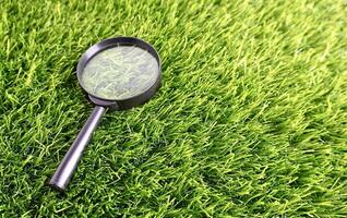 Magnifying glass with black frame and handle on top of grass field horizontal ratio background. Exploring nature themed photography. photo