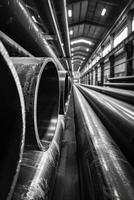 A long row of black pipes are stacked in a warehouse photo