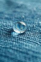 A small, clear, round droplet of water sits on a blue fabric photo