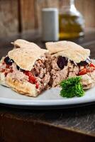 ciabatta bread sandwich with tuna, tomatoes and olives on plate photo