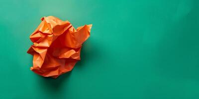 A crumpled orange piece of paper sits on a green background photo